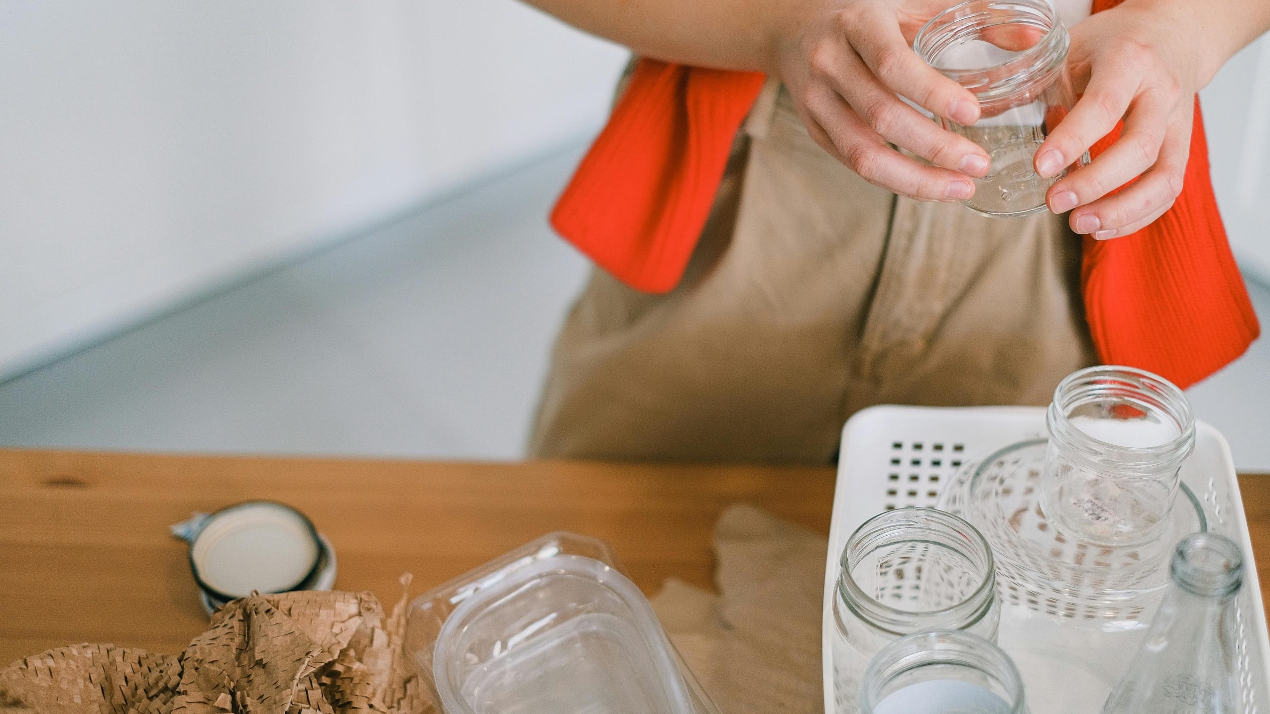Cilvēks virtuvē šķiro un atkārtoti izmanto stikla burciņas kā alternatīvu plastmasas iepakojumiem ilgtspējīgākai ikdienai.