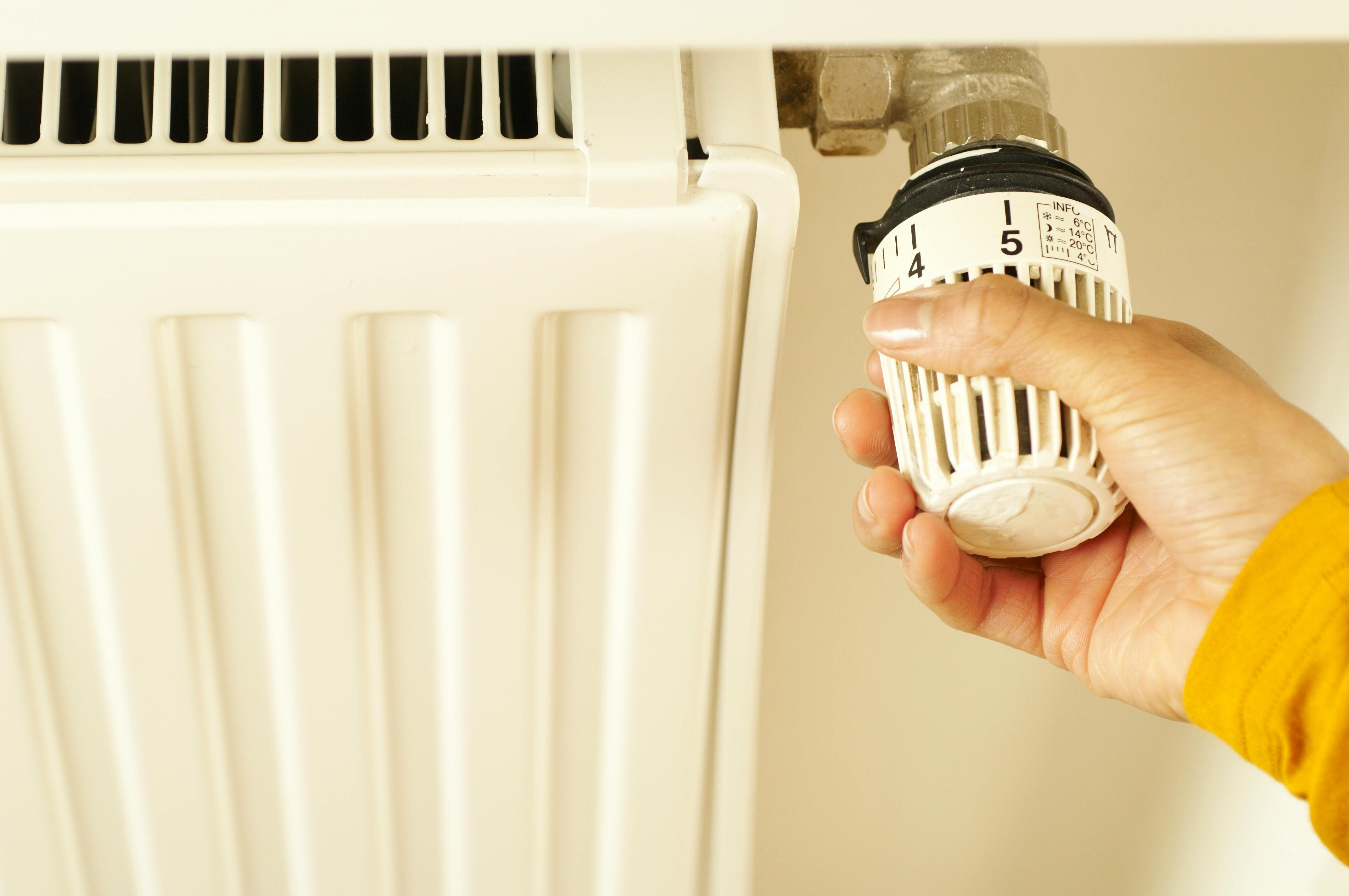 Roka pagriež radiatora termoregulatoru, lai pielāgotu temperatūru — tuvplāna skats ar fokusu uz apkures regulēšanu mājoklī