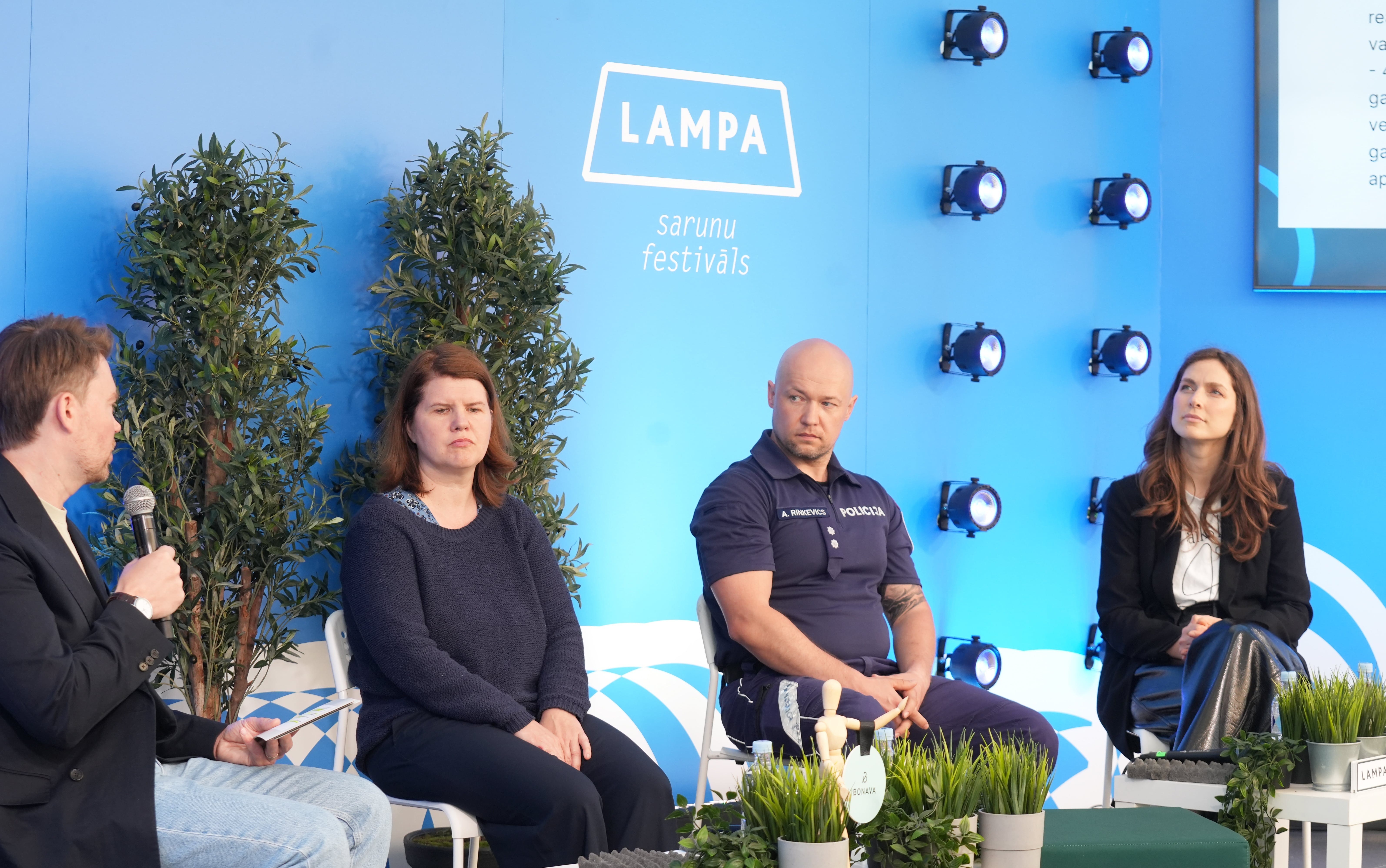 Diskusijas dalībnieki Sarunu festivālā LAMPA runā par bērnu drošību, sēžot uz skatuves zilā fona